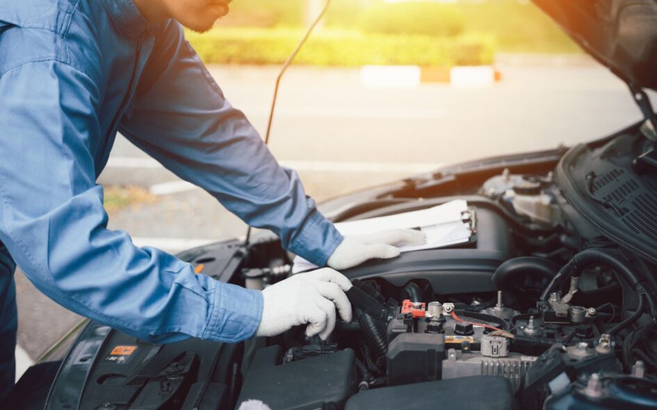 Close-up of a professional Asian mechanic's hand, in blue workwear, writing on a paper while working on a car in an auto repair shop.